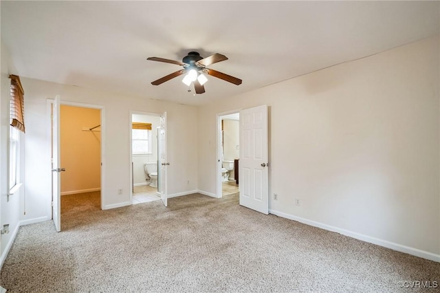 unfurnished bedroom featuring ensuite bathroom, a spacious closet, light colored carpet, a closet, and ceiling fan