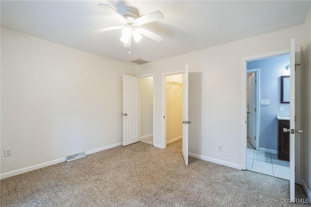 unfurnished bedroom with ensuite bath, ceiling fan, a spacious closet, light colored carpet, and a closet