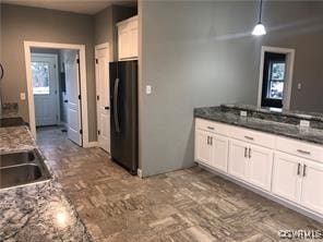 kitchen with black refrigerator, hanging light fixtures, white cabinetry, and dark stone countertops