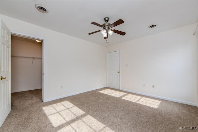 unfurnished bedroom featuring a spacious closet, light colored carpet, a closet, and ceiling fan