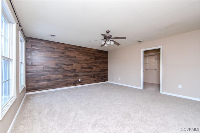 unfurnished room featuring ceiling fan, wooden walls, light colored carpet, and a healthy amount of sunlight