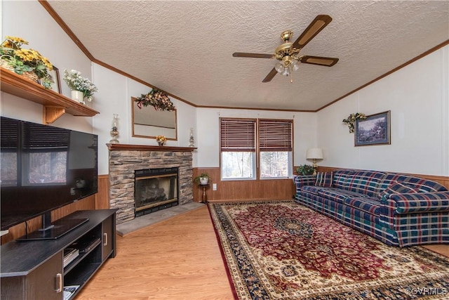 living room with wood-type flooring, a stone fireplace, ceiling fan, and a textured ceiling