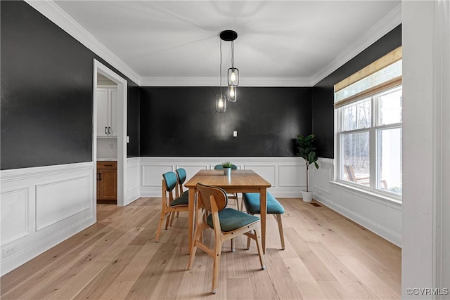 dining room featuring a wainscoted wall, crown molding, and light wood-style flooring