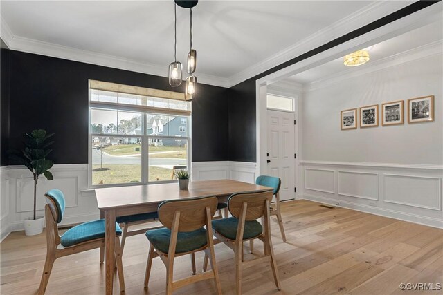 dining room with a wainscoted wall, crown molding, and light wood-style floors