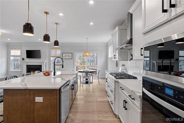 kitchen featuring stainless steel appliances, a sink, open floor plan, a lit fireplace, and wall chimney range hood