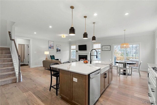 kitchen featuring light wood-style flooring, ornamental molding, a sink, a warm lit fireplace, and dishwasher