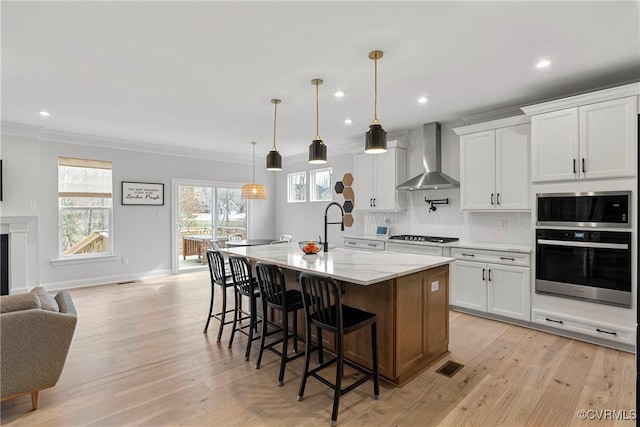 kitchen featuring wall chimney range hood, light wood-style flooring, decorative backsplash, and crown molding