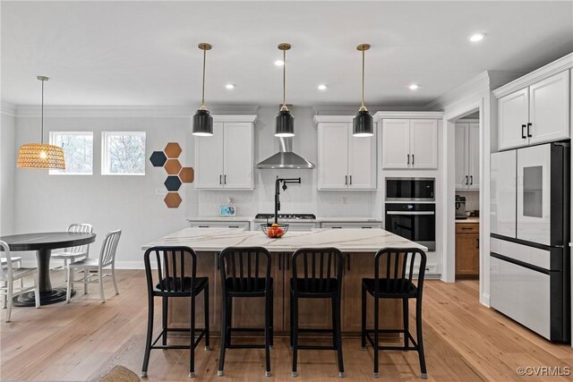 kitchen with refrigerator, stainless steel microwave, wall oven, white cabinets, and wall chimney range hood