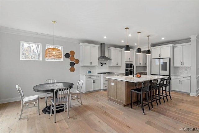 kitchen with a breakfast bar area, light wood finished floors, backsplash, white cabinets, and wall chimney range hood