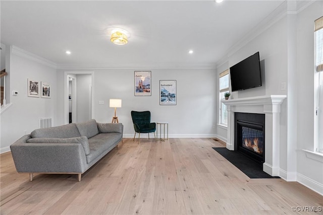 living room with light wood finished floors, a fireplace with flush hearth, visible vents, and crown molding