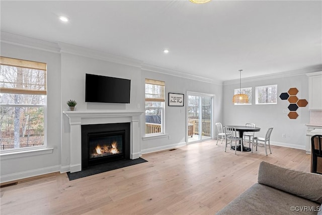 living area featuring a fireplace with flush hearth, visible vents, ornamental molding, and light wood-style flooring