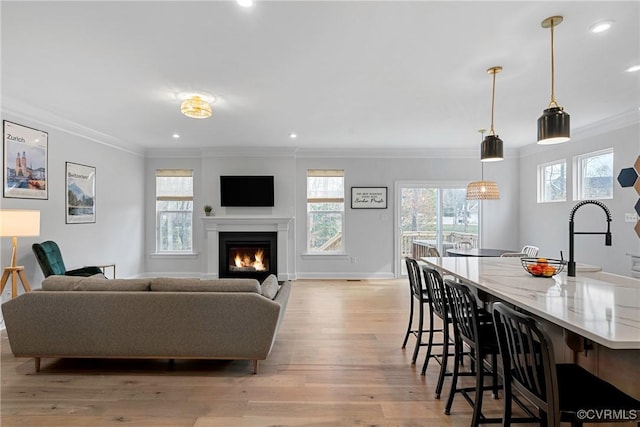 living room featuring light wood finished floors, baseboards, a glass covered fireplace, ornamental molding, and recessed lighting