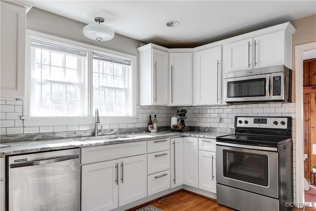 kitchen featuring sink, white cabinetry, stainless steel appliances, tasteful backsplash, and light stone countertops