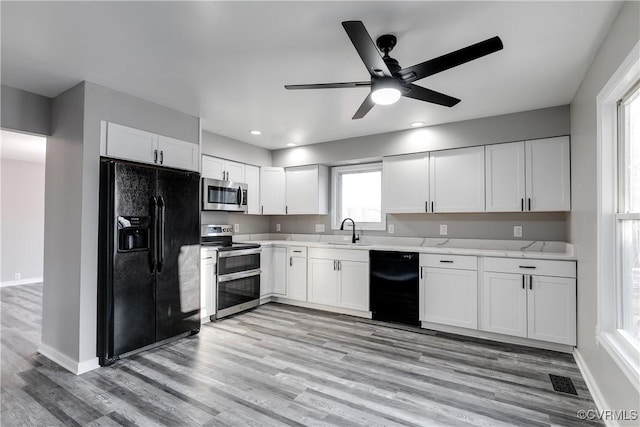 kitchen with white cabinetry, sink, black appliances, light stone countertops, and light hardwood / wood-style flooring