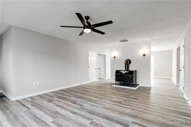 unfurnished living room with a textured ceiling, light hardwood / wood-style flooring, ceiling fan, and a wood stove