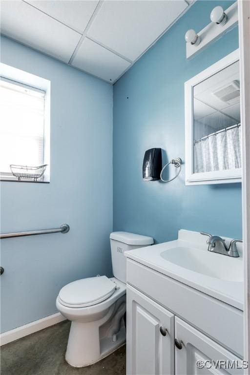 bathroom featuring concrete flooring, vanity, a drop ceiling, and toilet