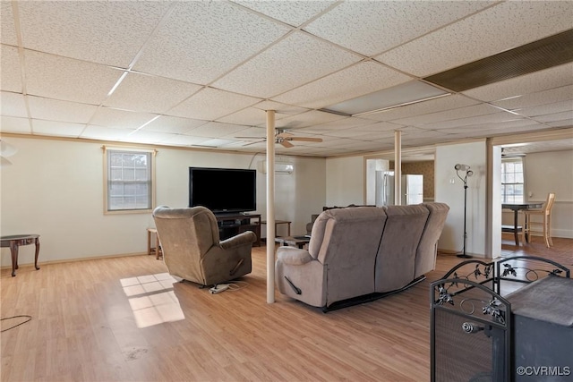 living room featuring ceiling fan, an AC wall unit, a drop ceiling, and light wood-type flooring