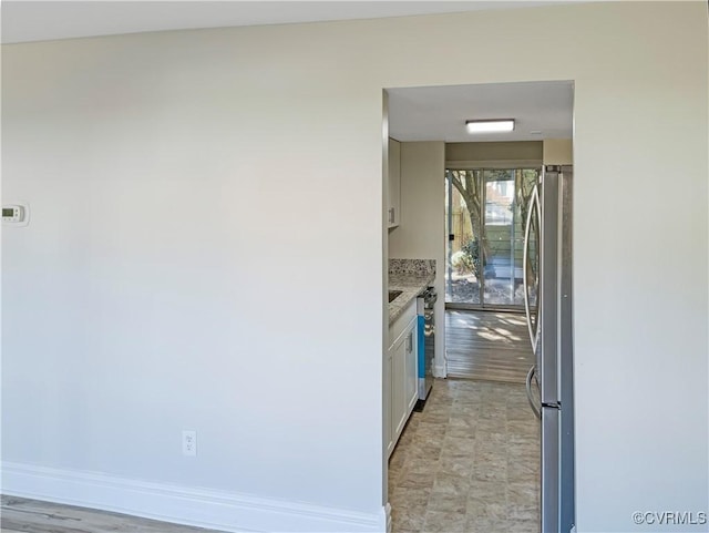 kitchen with stainless steel refrigerator, white cabinetry, and light stone counters