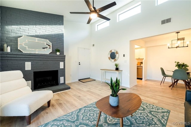 living room with wood-type flooring, ceiling fan with notable chandelier, a brick fireplace, and a high ceiling