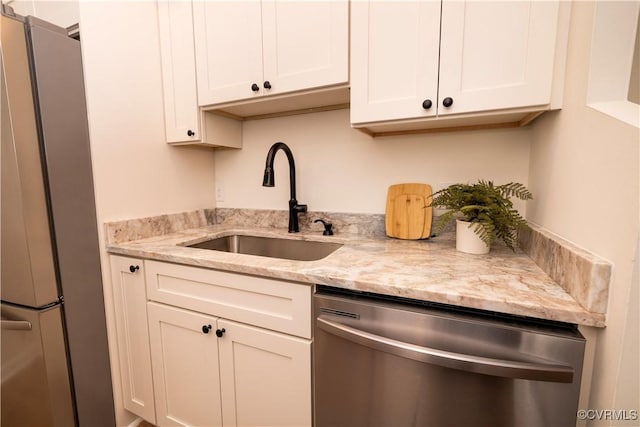 kitchen with stainless steel appliances, light stone countertops, sink, and white cabinets