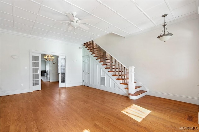 unfurnished living room with crown molding, ceiling fan with notable chandelier, hardwood / wood-style floors, and french doors