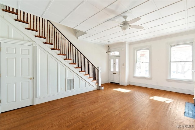 entryway with wood-type flooring, ornamental molding, and ceiling fan