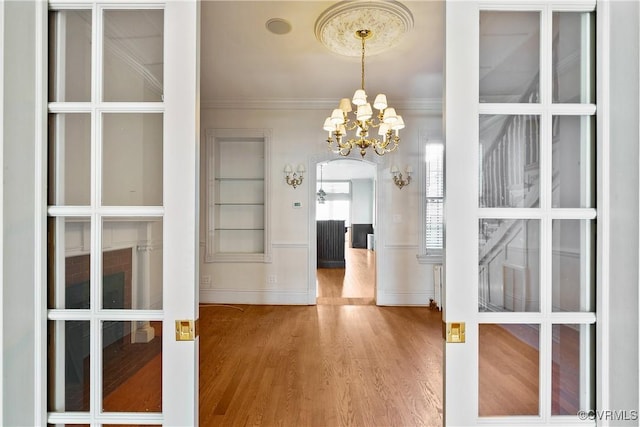 unfurnished dining area featuring an inviting chandelier, hardwood / wood-style floors, ornamental molding, and french doors