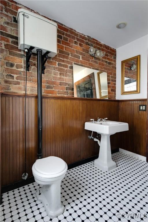 bathroom featuring toilet, brick wall, and wood walls