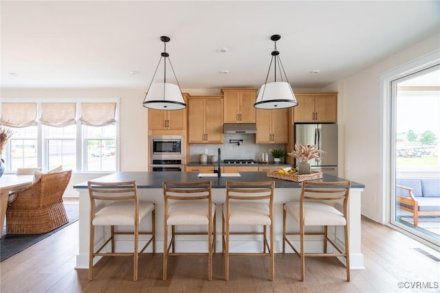 kitchen featuring stainless steel appliances, a center island with sink, backsplash, and decorative light fixtures