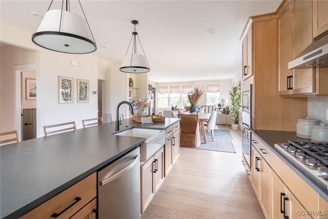 kitchen featuring appliances with stainless steel finishes, decorative light fixtures, sink, backsplash, and light hardwood / wood-style flooring