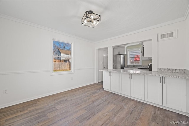 kitchen with stainless steel fridge, white cabinetry, light stone counters, wood-type flooring, and ornamental molding