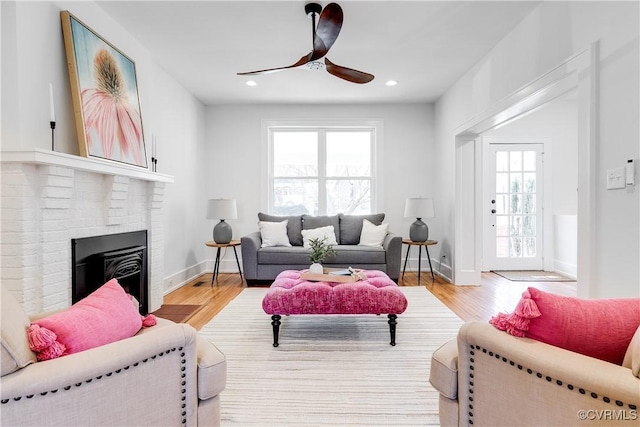 living room with ceiling fan, a brick fireplace, and light wood-type flooring