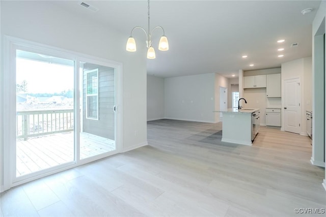 interior space featuring sink, a notable chandelier, an island with sink, white cabinets, and decorative light fixtures