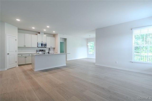 kitchen with sink, light hardwood / wood-style flooring, white cabinetry, a kitchen island with sink, and stainless steel appliances