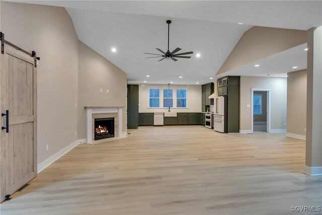 unfurnished living room featuring ceiling fan, a barn door, sink, and light wood-type flooring