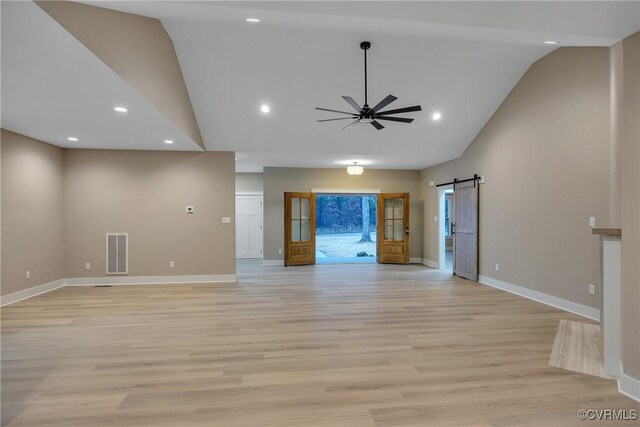 unfurnished living room featuring ceiling fan, a barn door, high vaulted ceiling, and light hardwood / wood-style floors