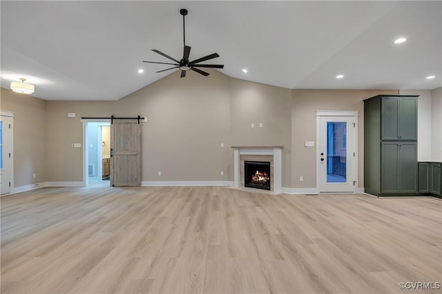 unfurnished living room with ceiling fan, lofted ceiling, a barn door, and light hardwood / wood-style flooring