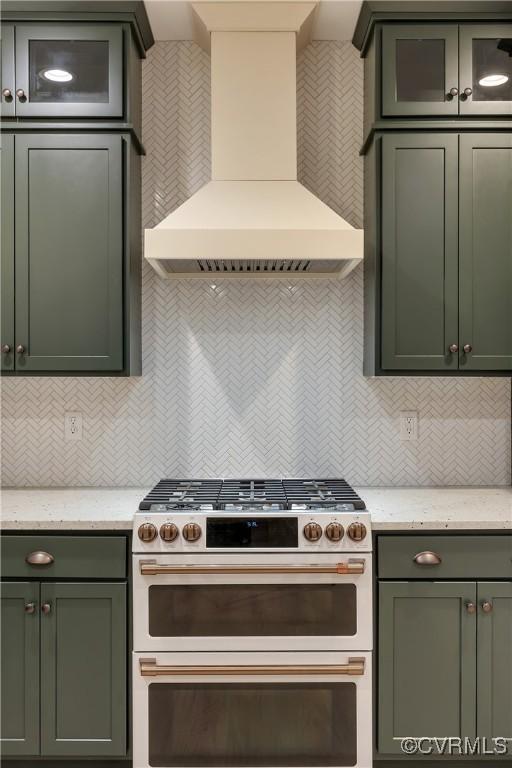 kitchen with double oven range, light stone countertops, green cabinets, and custom range hood