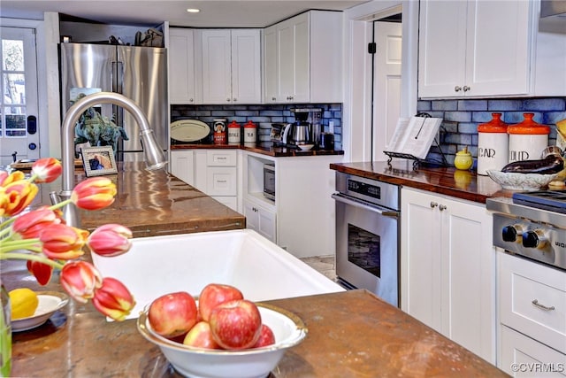 kitchen featuring stainless steel appliances, butcher block countertops, decorative backsplash, and white cabinets