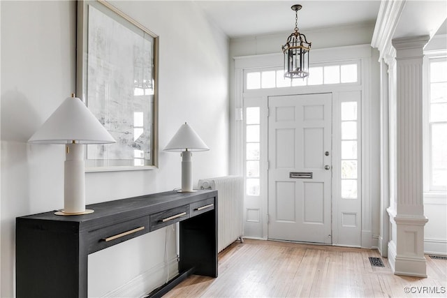 entrance foyer with decorative columns, radiator heating unit, and light wood-type flooring