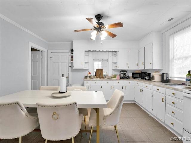 kitchen with light tile patterned floors, ceiling fan, white cabinetry, a kitchen breakfast bar, and ornamental molding