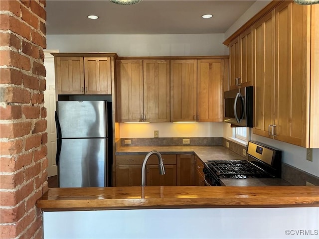 kitchen featuring brick wall, stainless steel appliances, sink, and wooden counters