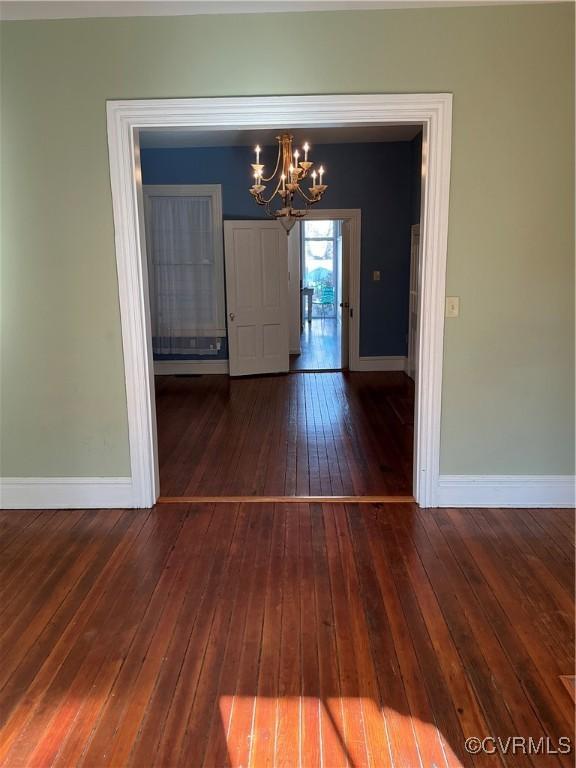 unfurnished dining area featuring an inviting chandelier and dark wood-type flooring