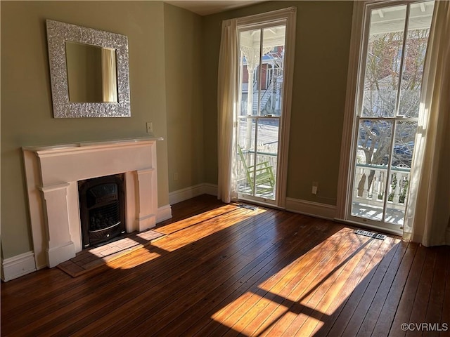 unfurnished living room featuring a wealth of natural light, wood-type flooring, visible vents, and baseboards