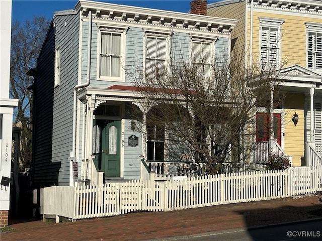 italianate house featuring a fenced front yard and a chimney