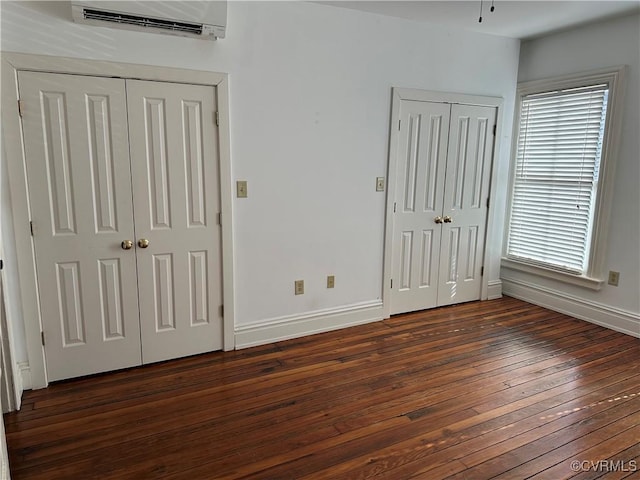 unfurnished bedroom featuring dark wood-type flooring, a wall mounted AC, two closets, and baseboards