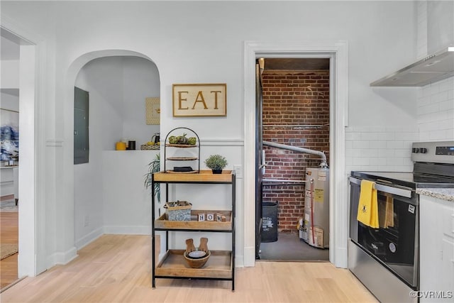 kitchen featuring water heater, stainless steel range with electric stovetop, electric panel, wall chimney range hood, and light wood-type flooring