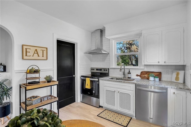 kitchen with wall chimney exhaust hood, stainless steel appliances, sink, and white cabinets