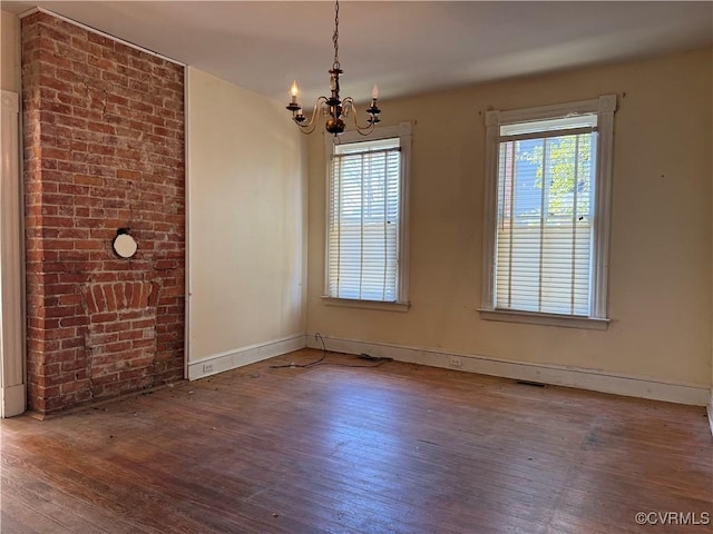 empty room with baseboards, wood-type flooring, a notable chandelier, and visible vents