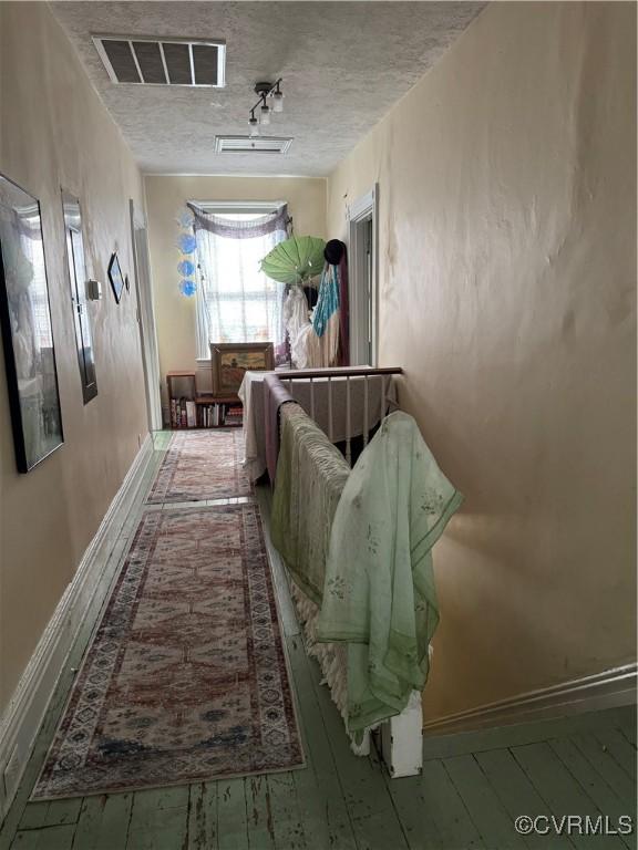 hall featuring visible vents, baseboards, a textured ceiling, and hardwood / wood-style flooring